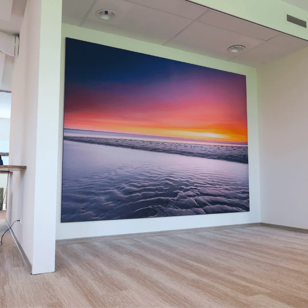 Groot wanddoek met een strand bij zonsondergang in paars en oranje, op een lichte kantoorwand
