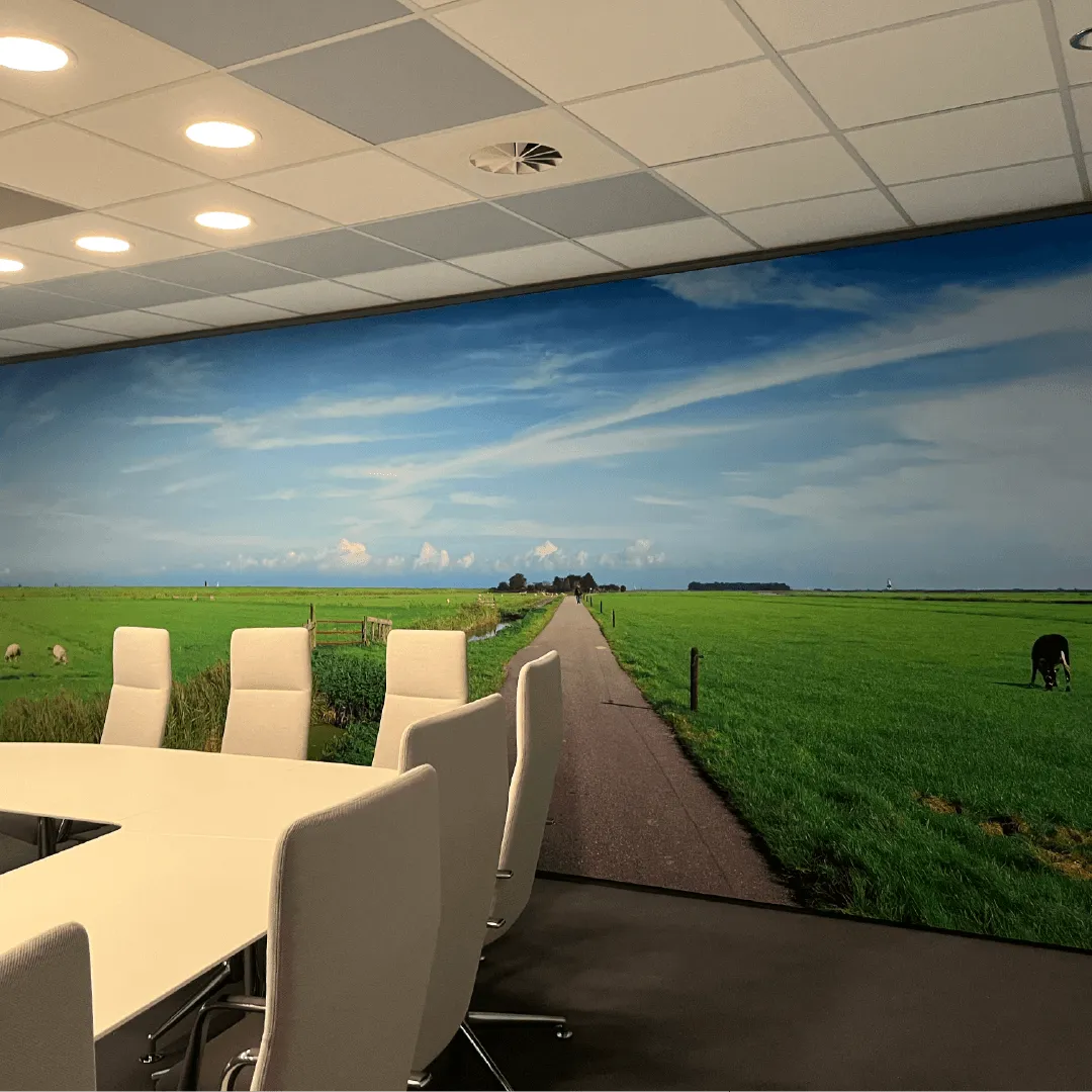 Vergaderruimte met een wandvullend doek van een polderpad met weiland en luchten, van muur tot muur achter de vergadertafel