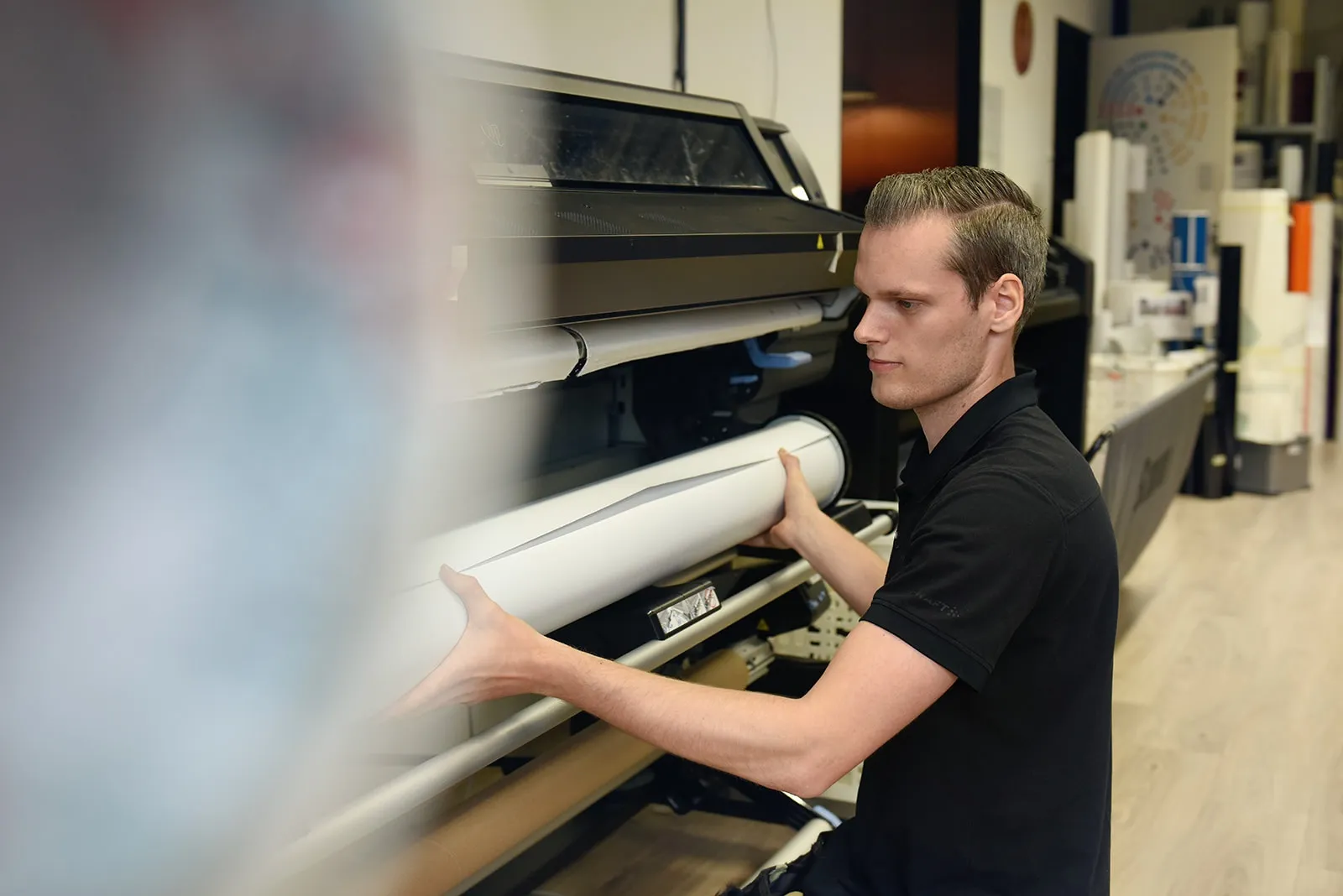 Een rol materiaal wordt in de grote printer in de werkplaats geladen